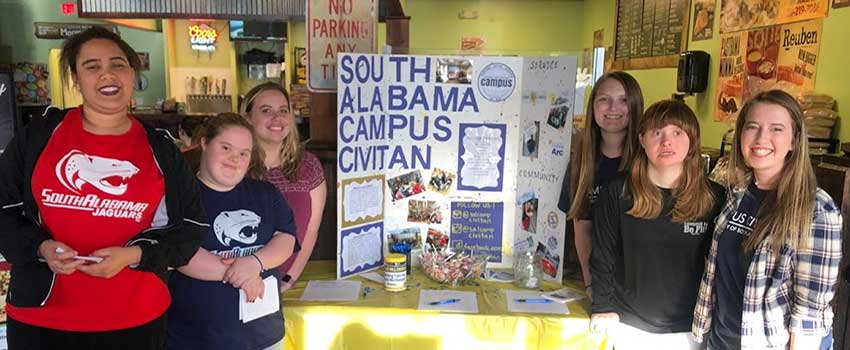 Students and Mentors who are part of the South Alabama Civitan standing at table at recruiting drive and fundraiser event.